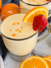 A glass mug of Orange Julius with a strawberry and a slice of orange on the side.