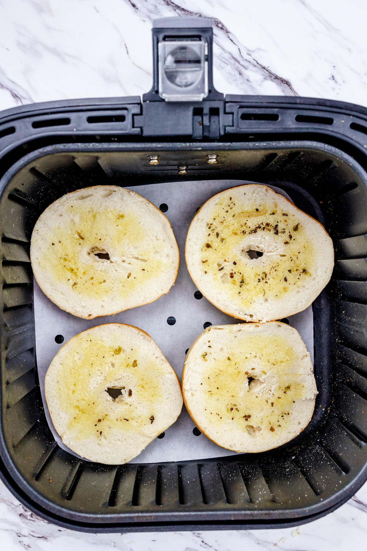 Top view of oiled bagel slices being toasted in the air fryer.