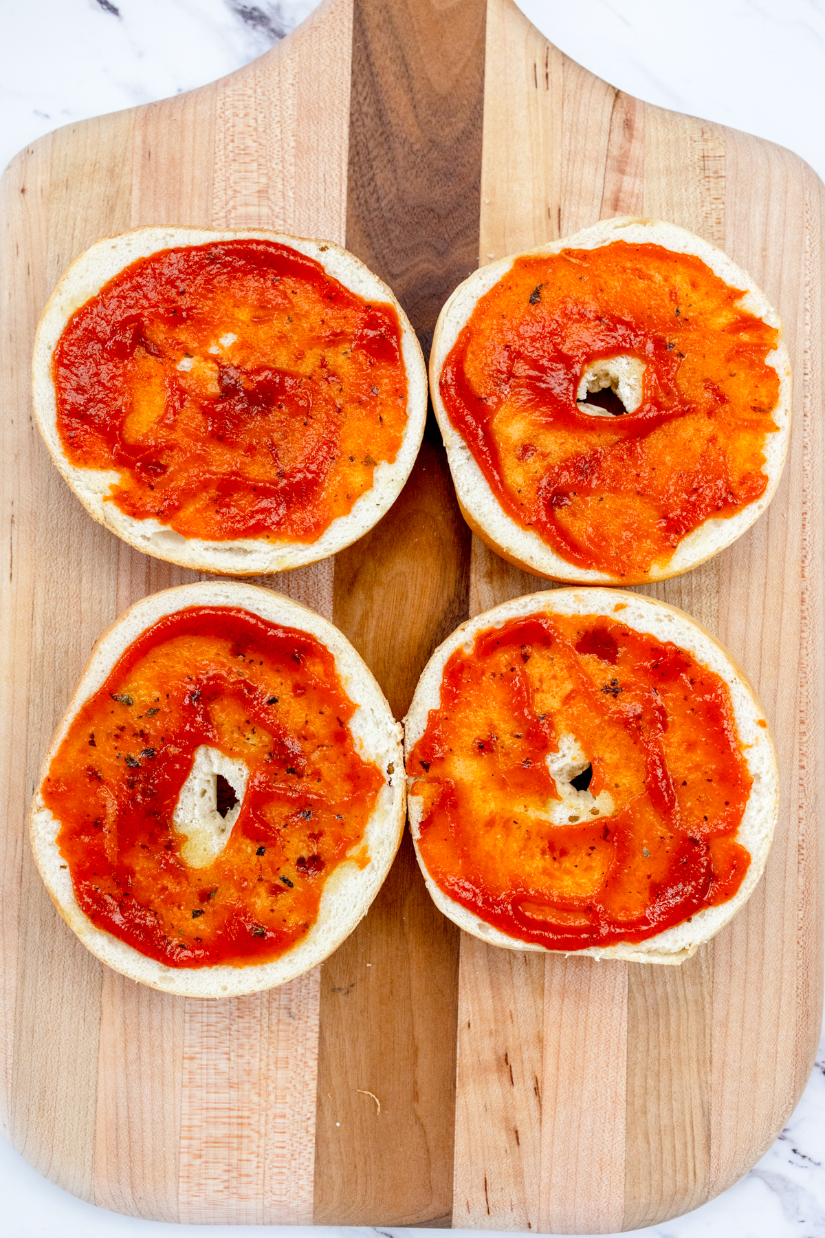 Top view of bagel slices with pizza sauce spread on them.