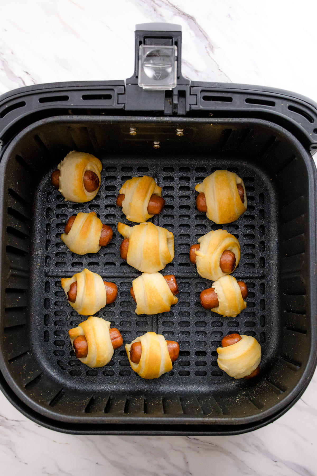 Top view of 12 cooked Pigs in a Blanket in an air fryer basket.