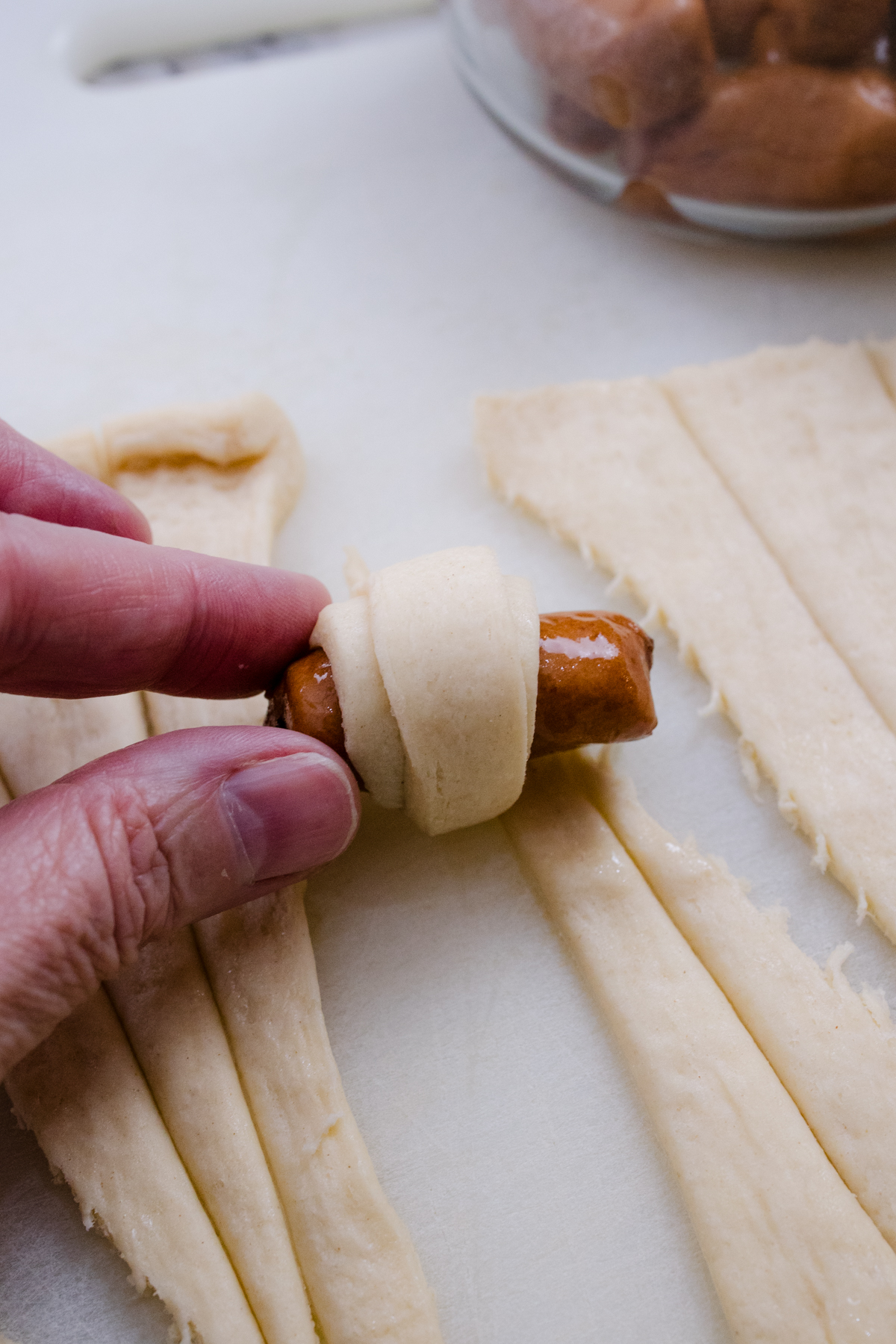 Close up view of someone rolling a Lil Smokie in sliced crescent roll pastry.