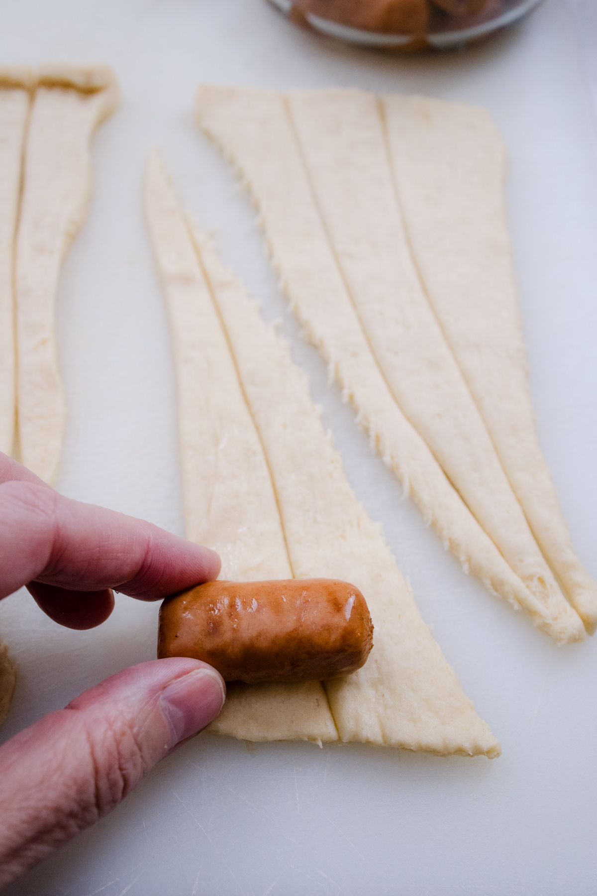 Close up view of someone placing a Lil Smokie onto the sliced crescent roll pastry.