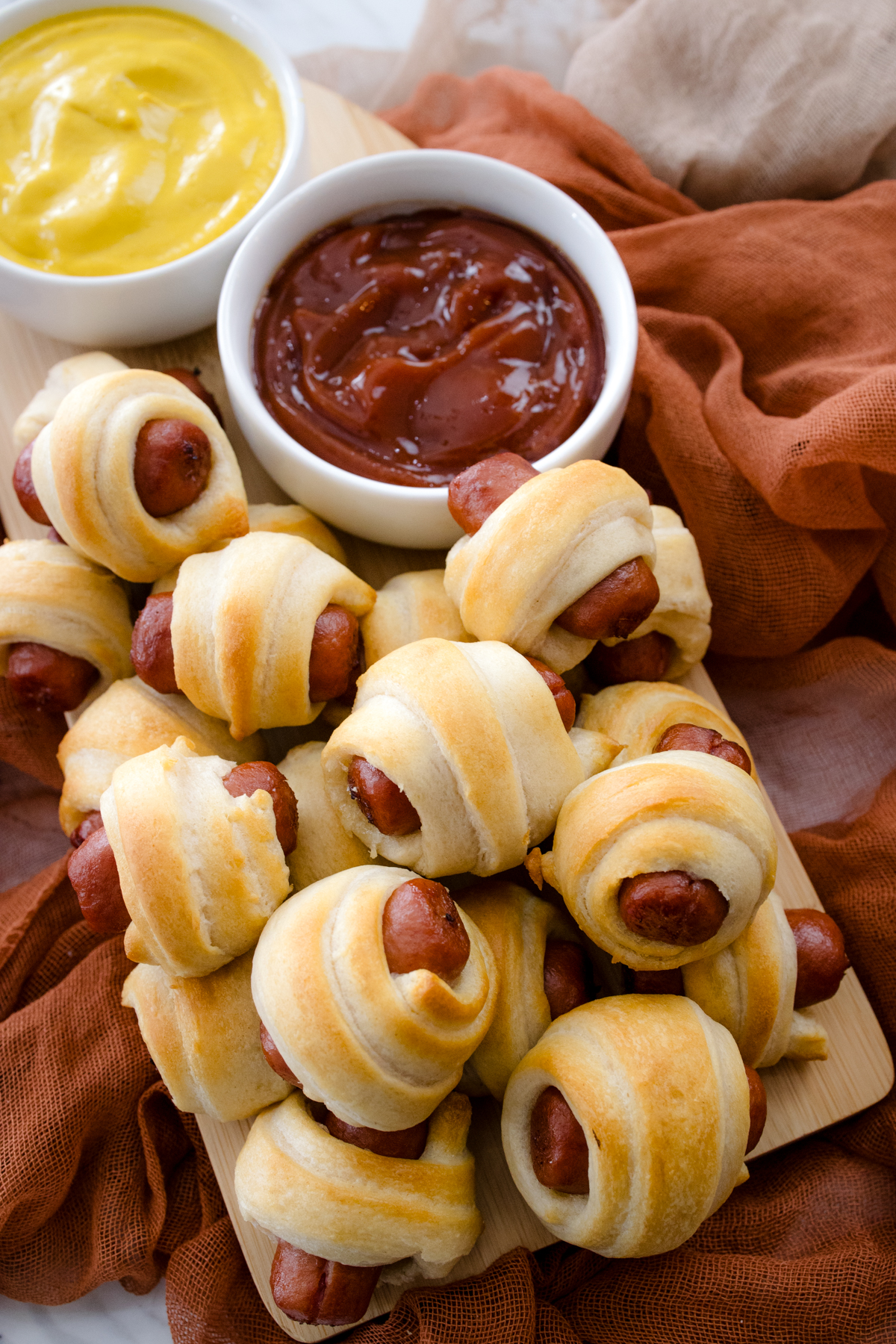 Top view of air fried Pigs in a Blanket on a countertop with decorations next to ramekins filled with tomato ketchup and mustard.