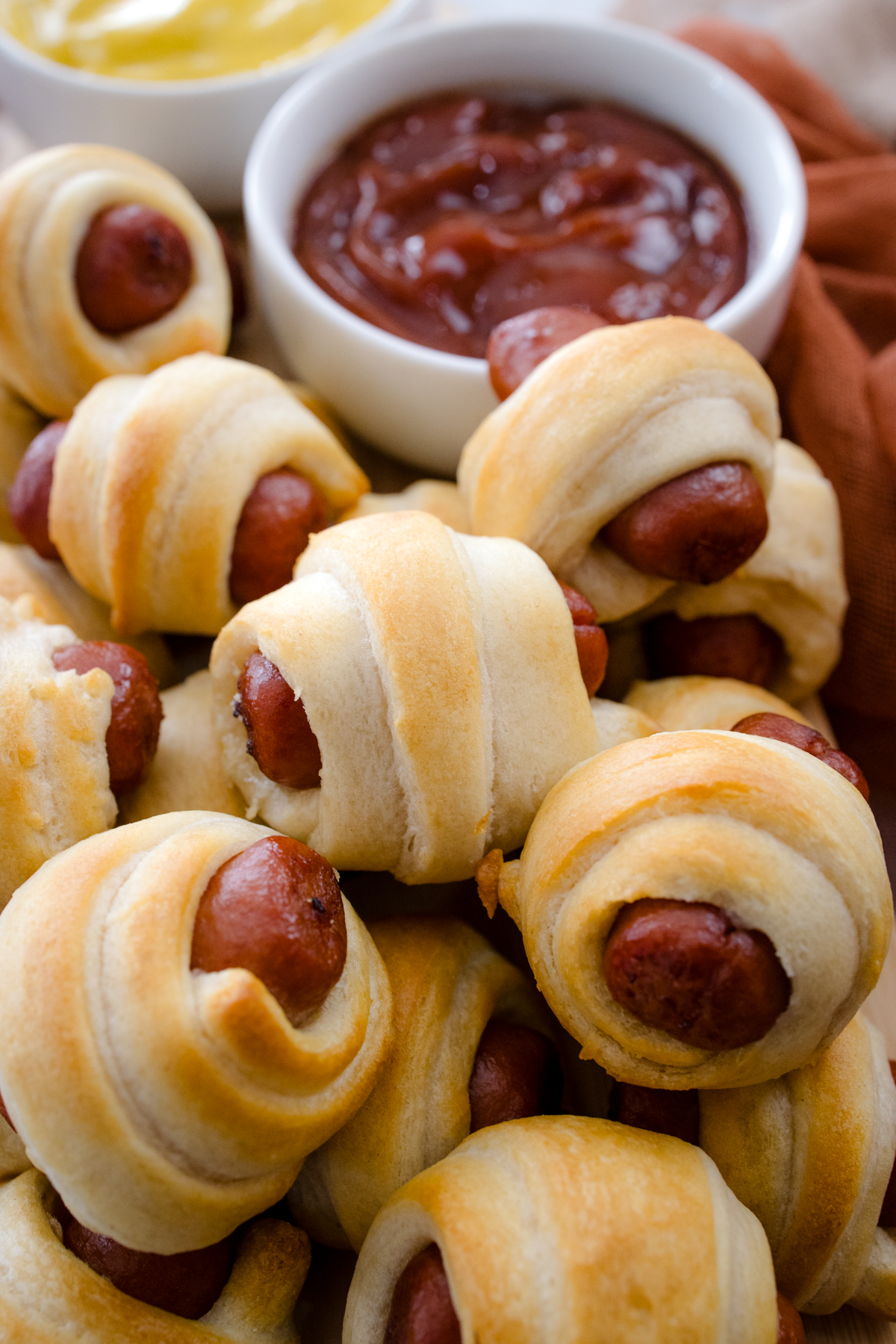 Close up view of air fried Pigs in a Blanket on a countertop with decorations next to ramekins filled with tomato ketchup and mustard.