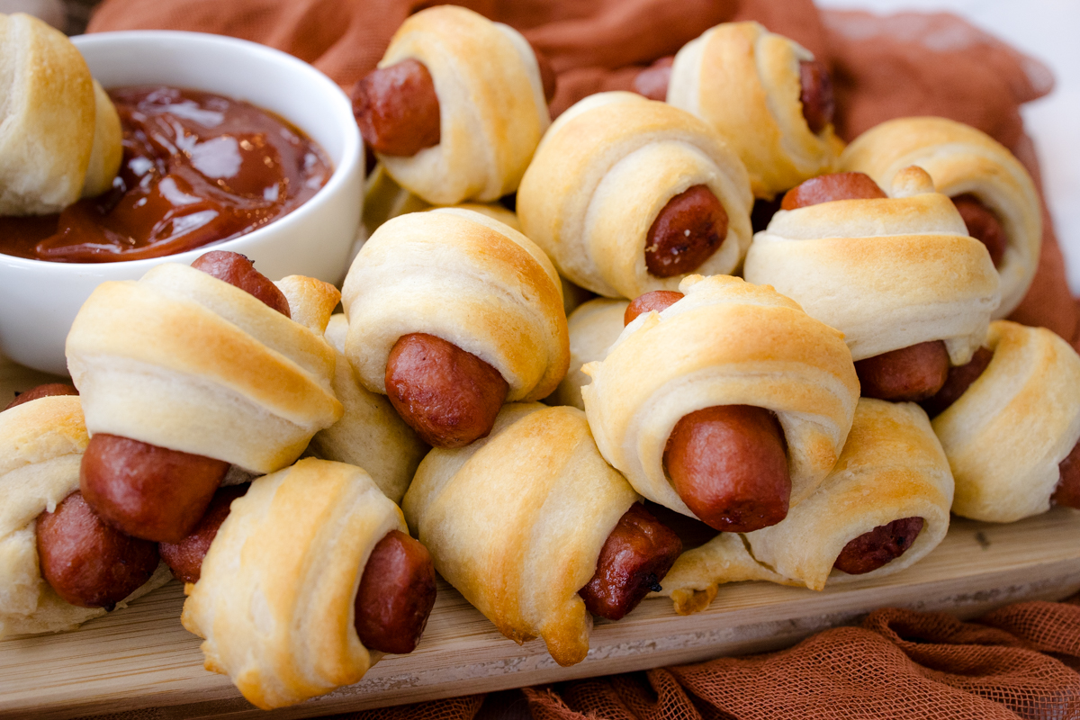 Close up view of air fried Pigs in a Blanket on a countertop with decorations next to a ramekin filled with tomato ketchup.