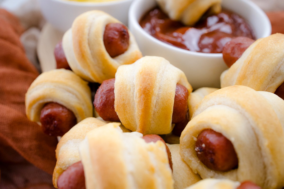 Close up view of air fried Pigs in a Blanket on a countertop with decorations next to a ramekin filled with tomato ketchup.