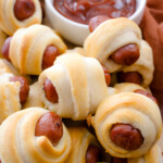 Close up view of air fried Pigs in a Blanket on a countertop with decorations next to a ramekin filled with tomato ketchup.