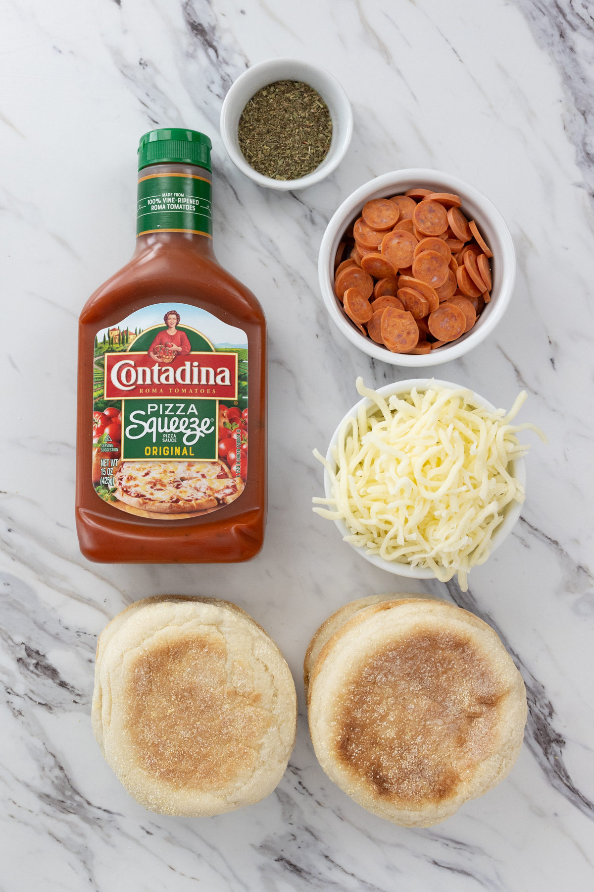 Top view of ingredients needed to make Air Fryer English Muffin Pizzas in small bowls on a baking tray.