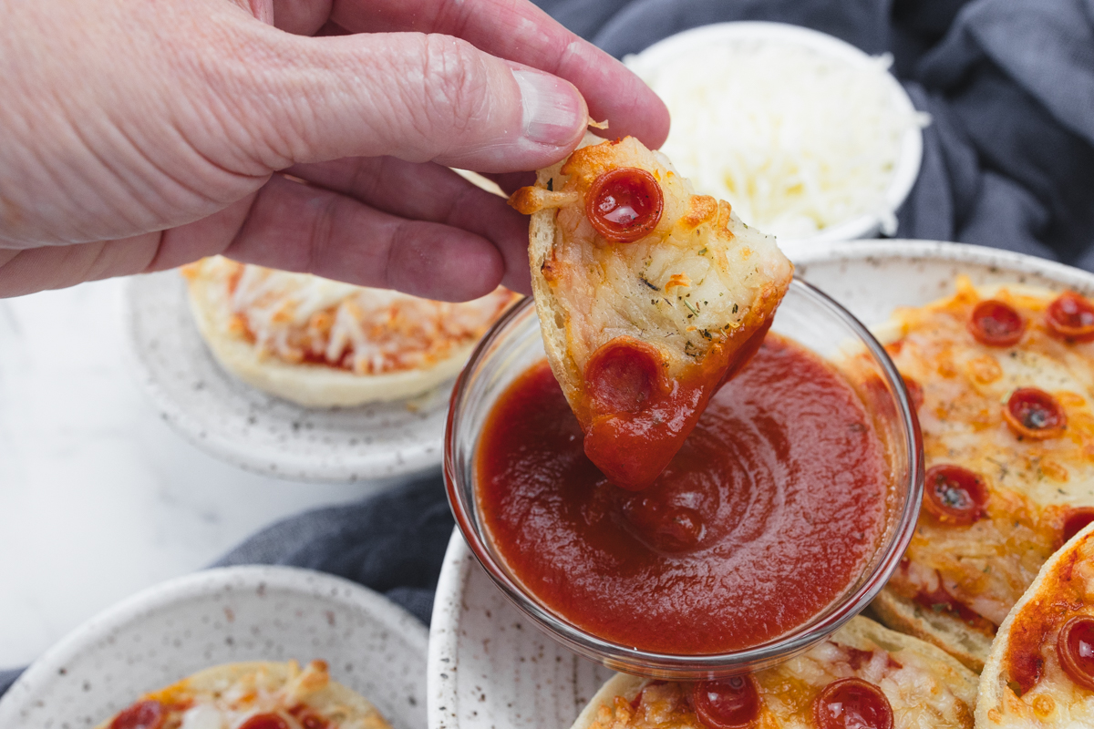 Close up view of sliced English Muffin Pizzas being dipped in sauce.