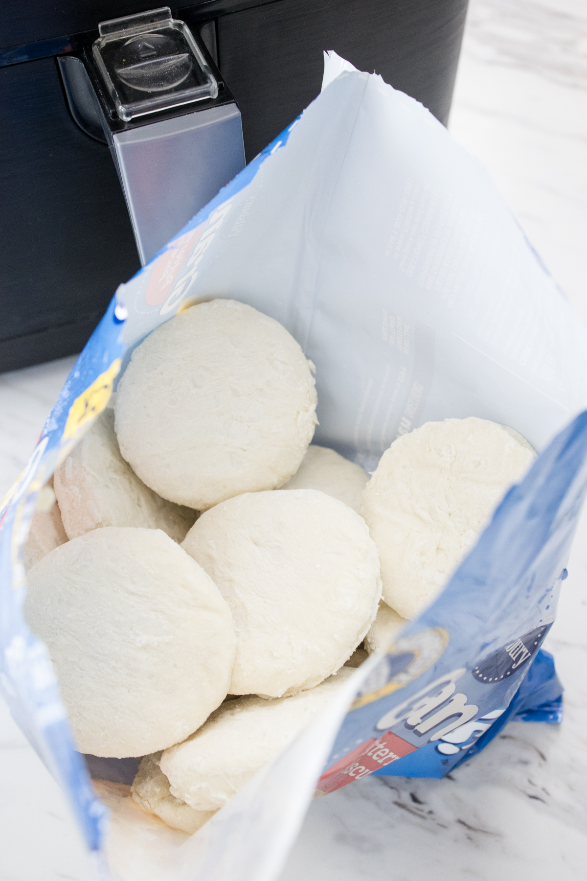 Close up view of an opened bag of Pillsbury Grands biscuits in front of an air fryer.