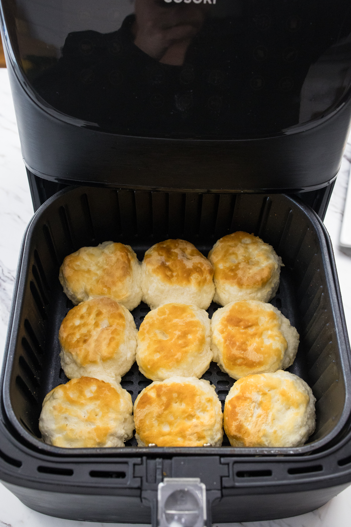 Top view of an open air fryer with cooked biscuits in it.