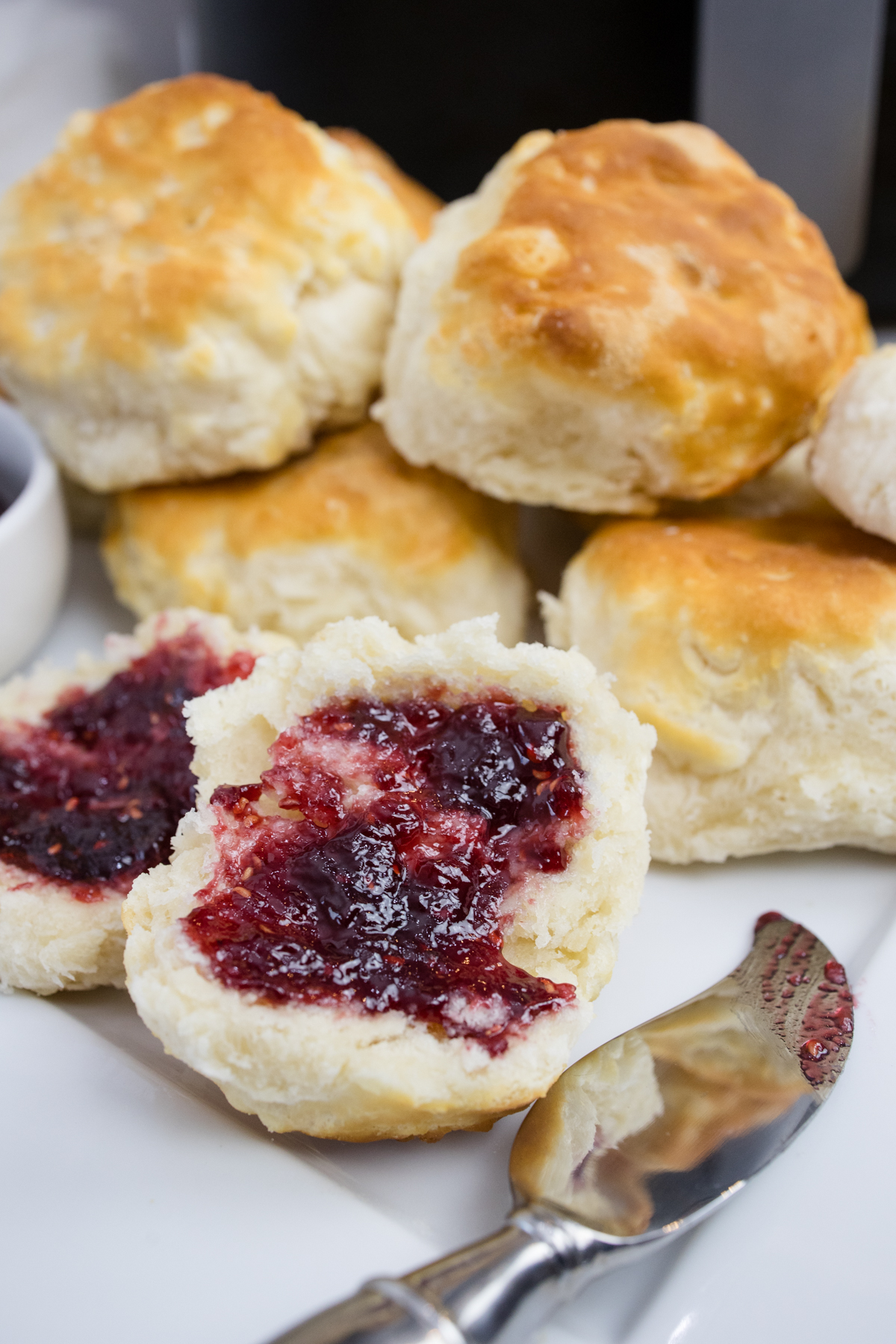 Top view of cooked biscuits on a white surface next to a ramakin of jam and a knife.