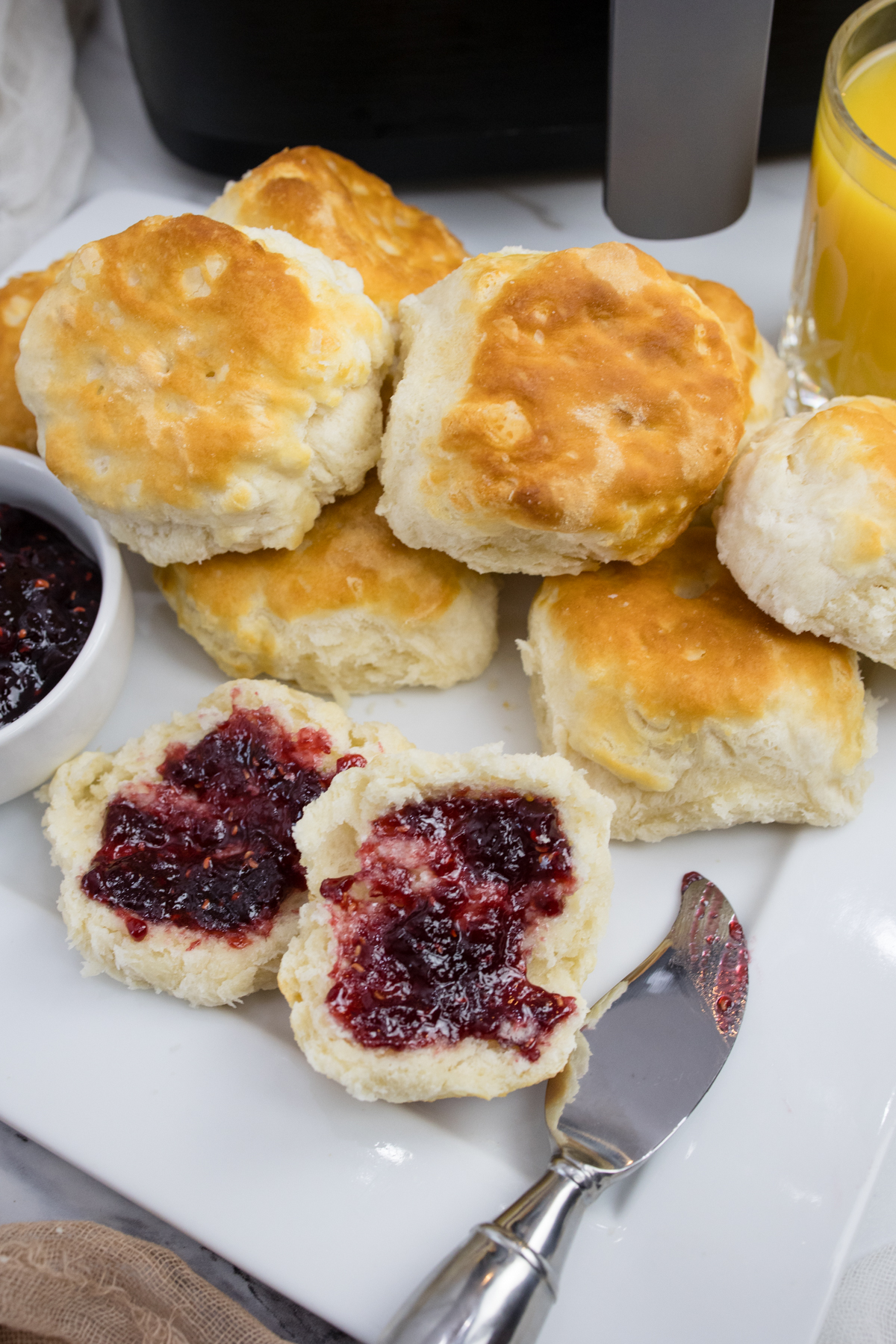 Top view of cooked biscuits on a white surface next to a ramakin of jam and a knife.