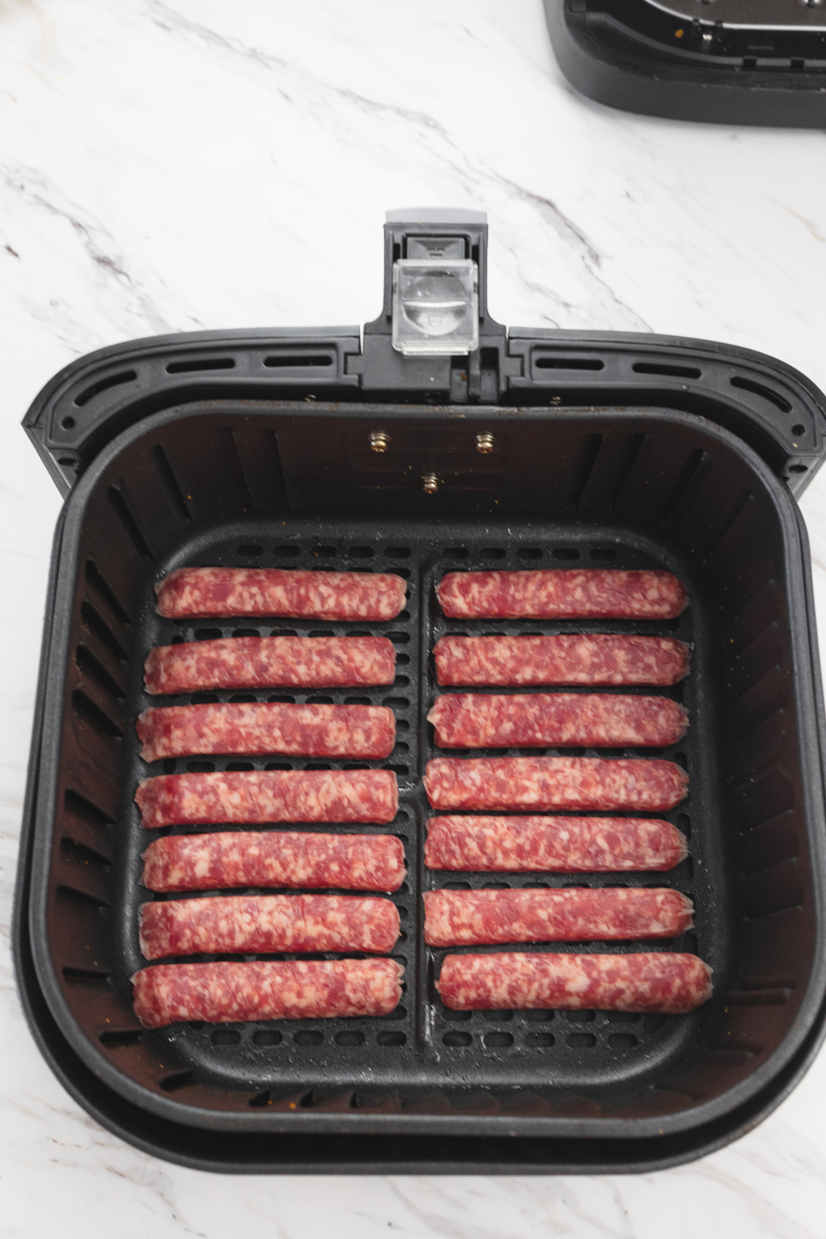 A top view of 14 uncooked link sausages in an open air fryer basket.