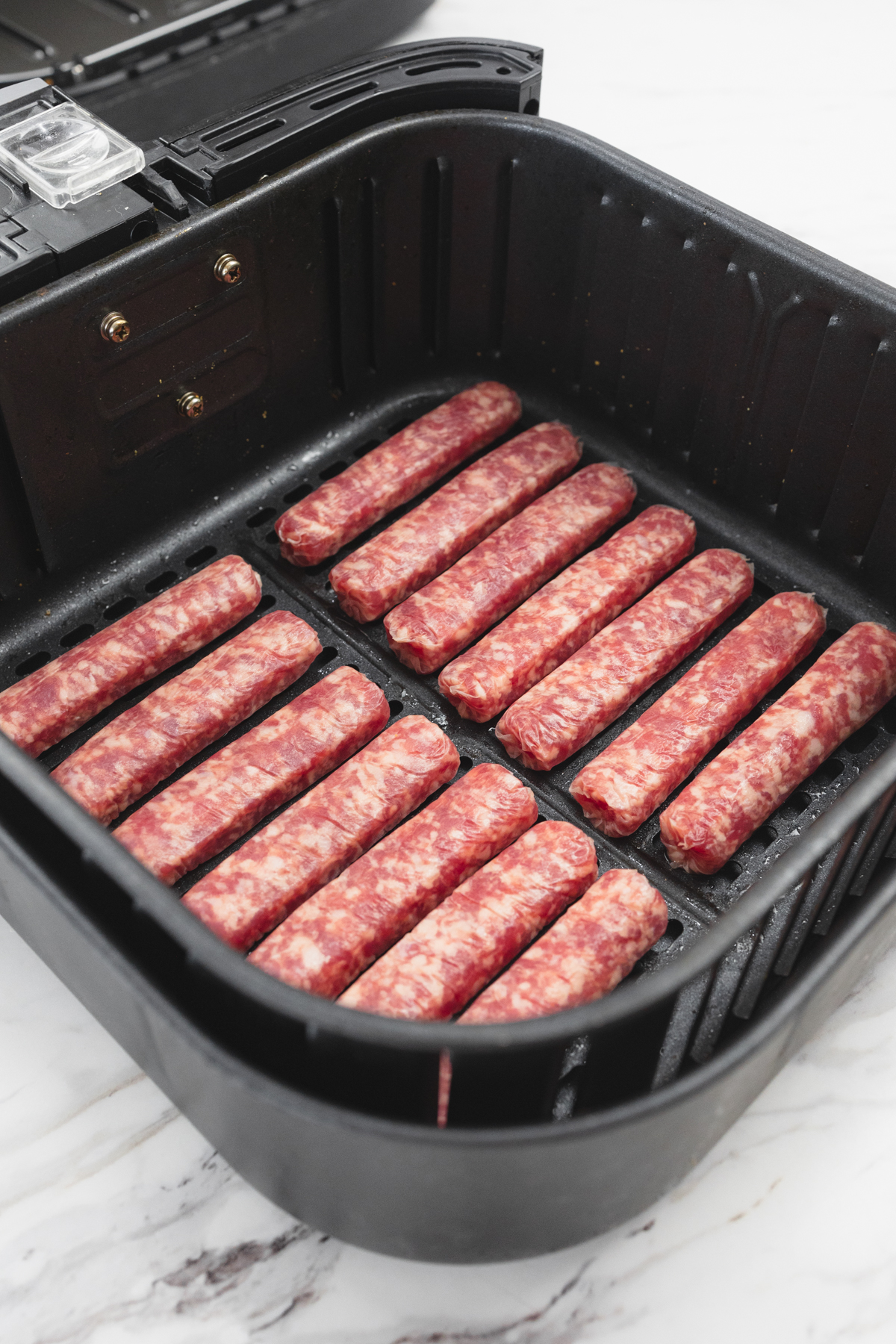 A close view of 14 uncooked link sausages in an open air fryer basket.