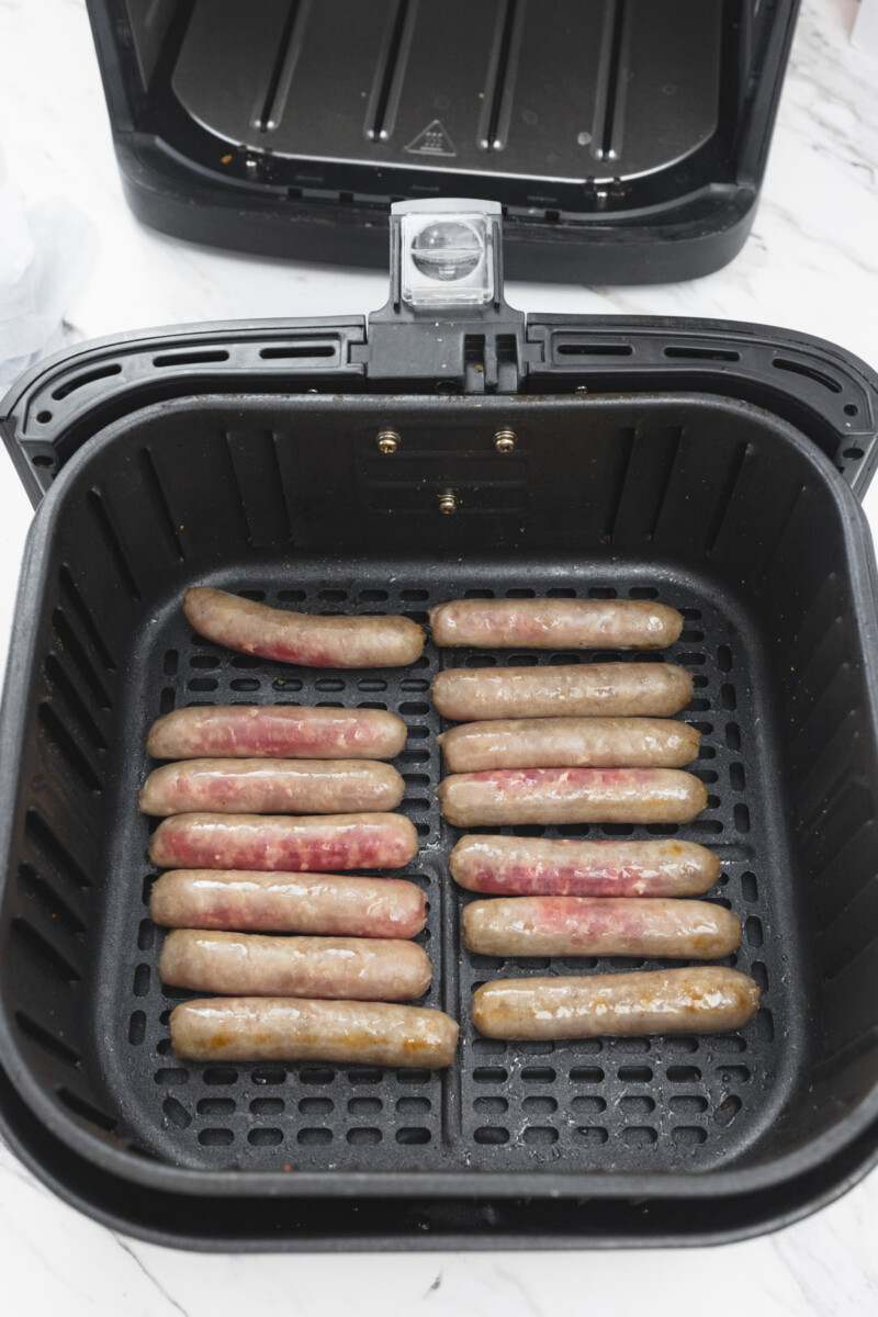 A top view of 14 link sausages in an open air fryer basket halfway through cooking.