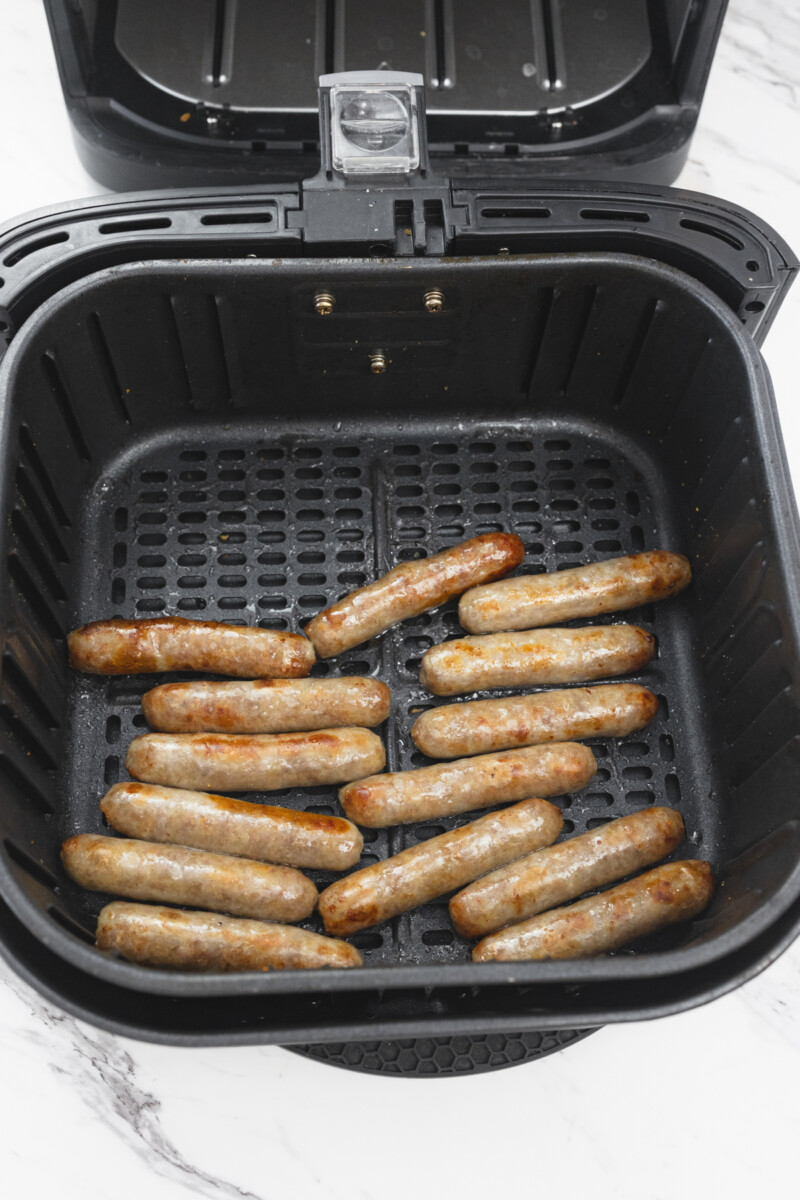 A top view of 14 cooked link sausages in an open air fryer basket.