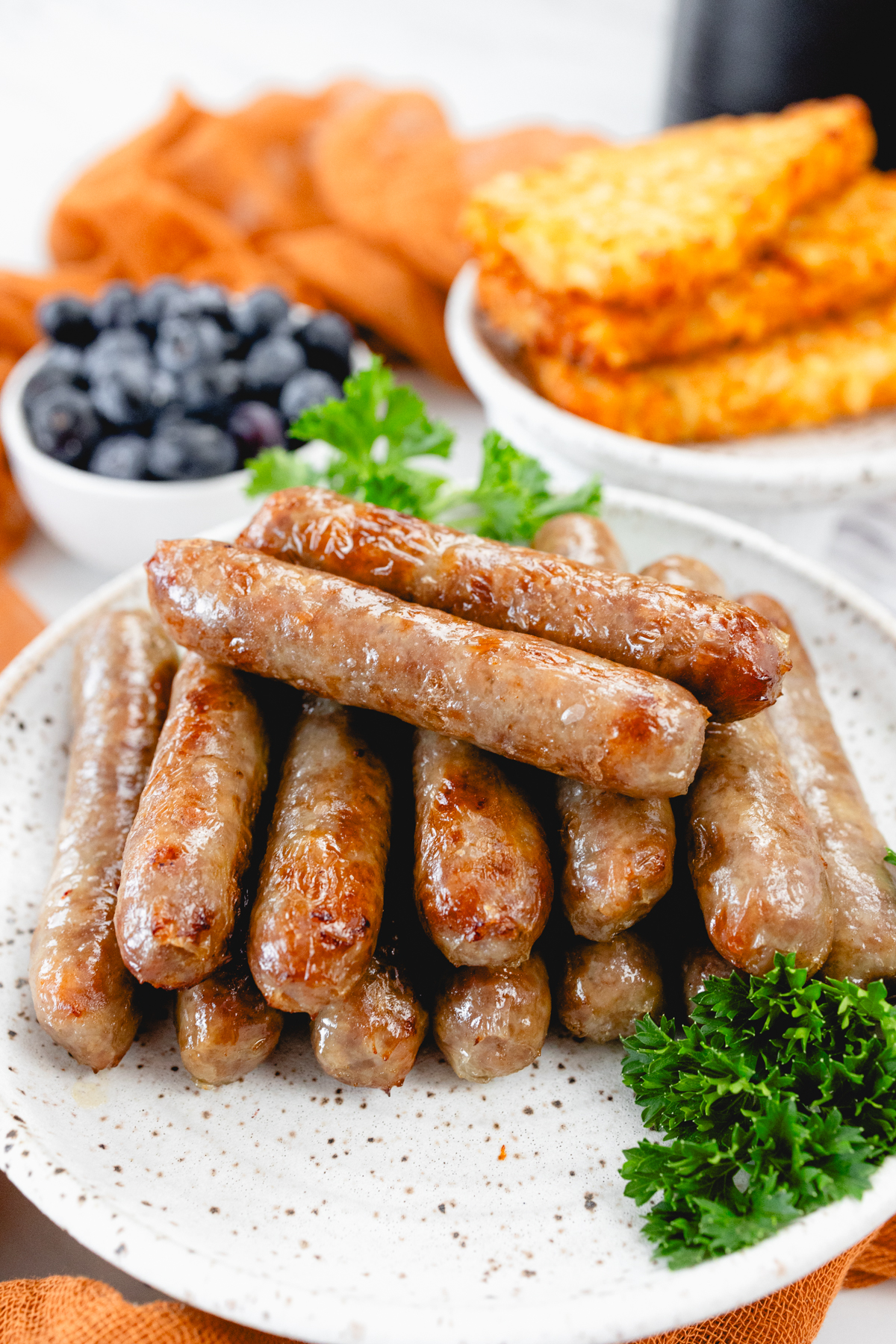 A close up view of 14 link sausages on a white plate with other breakfast items on the table.