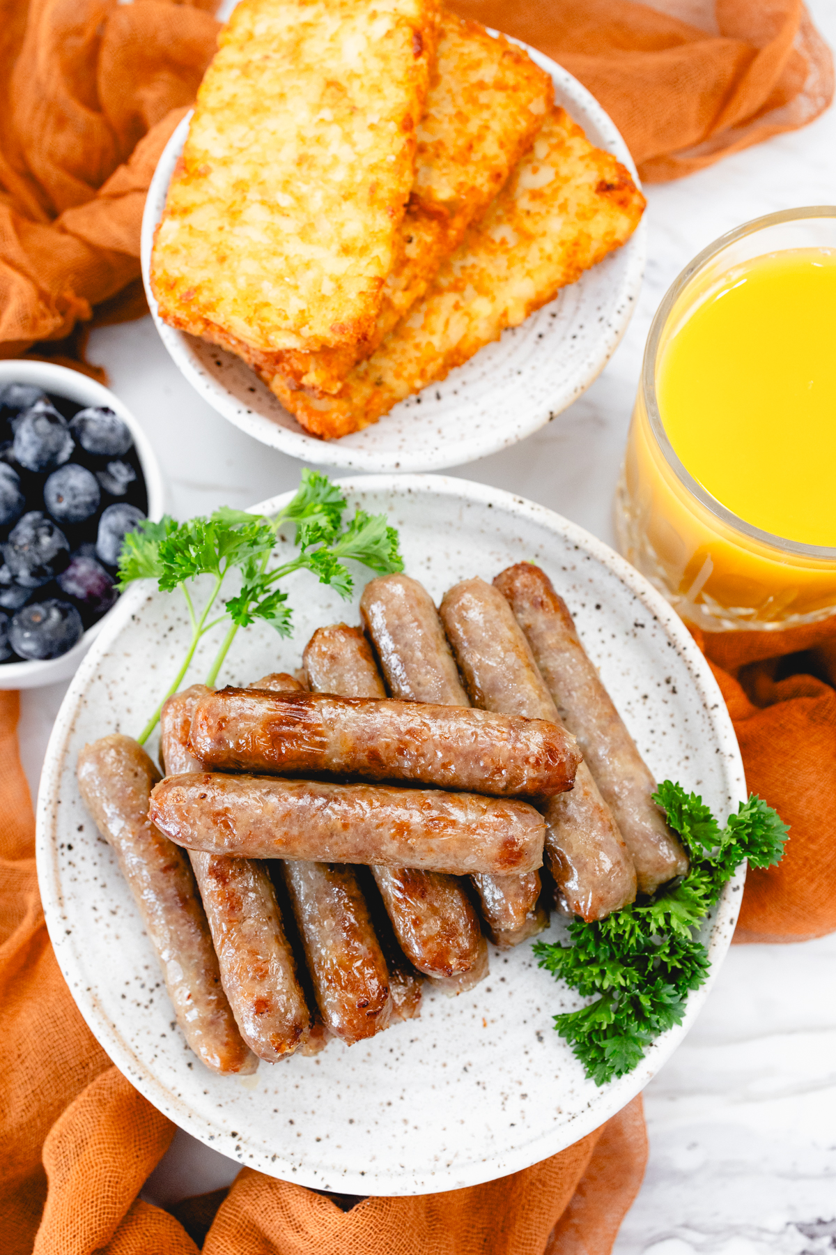 A top view of 14 link sausages on a white plate with other breakfast items on the table.