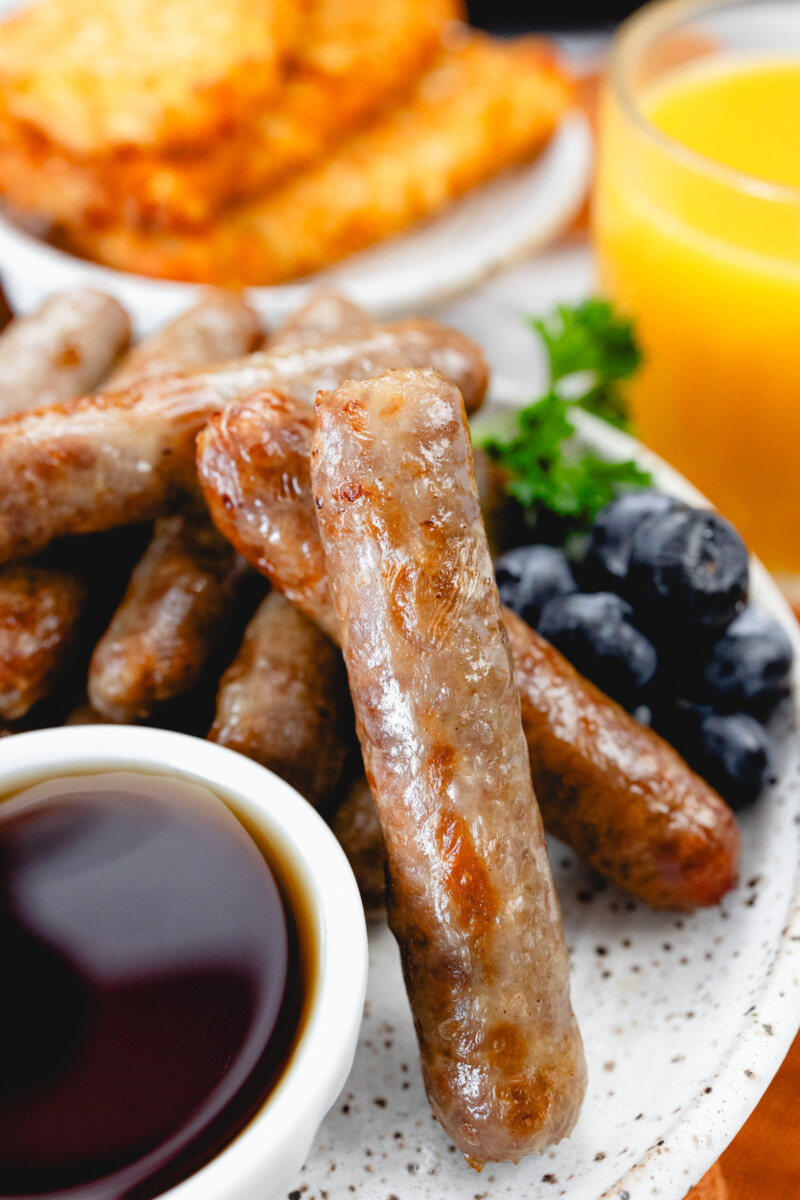 A close up view of link sausages on a white plate with berries and gravy.