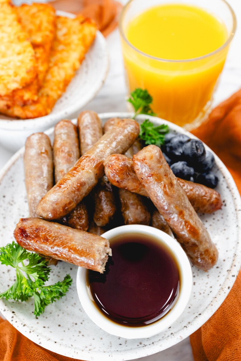 A top view of link sausages on a white plate with berries and gravy next to other breakfast items on a table.