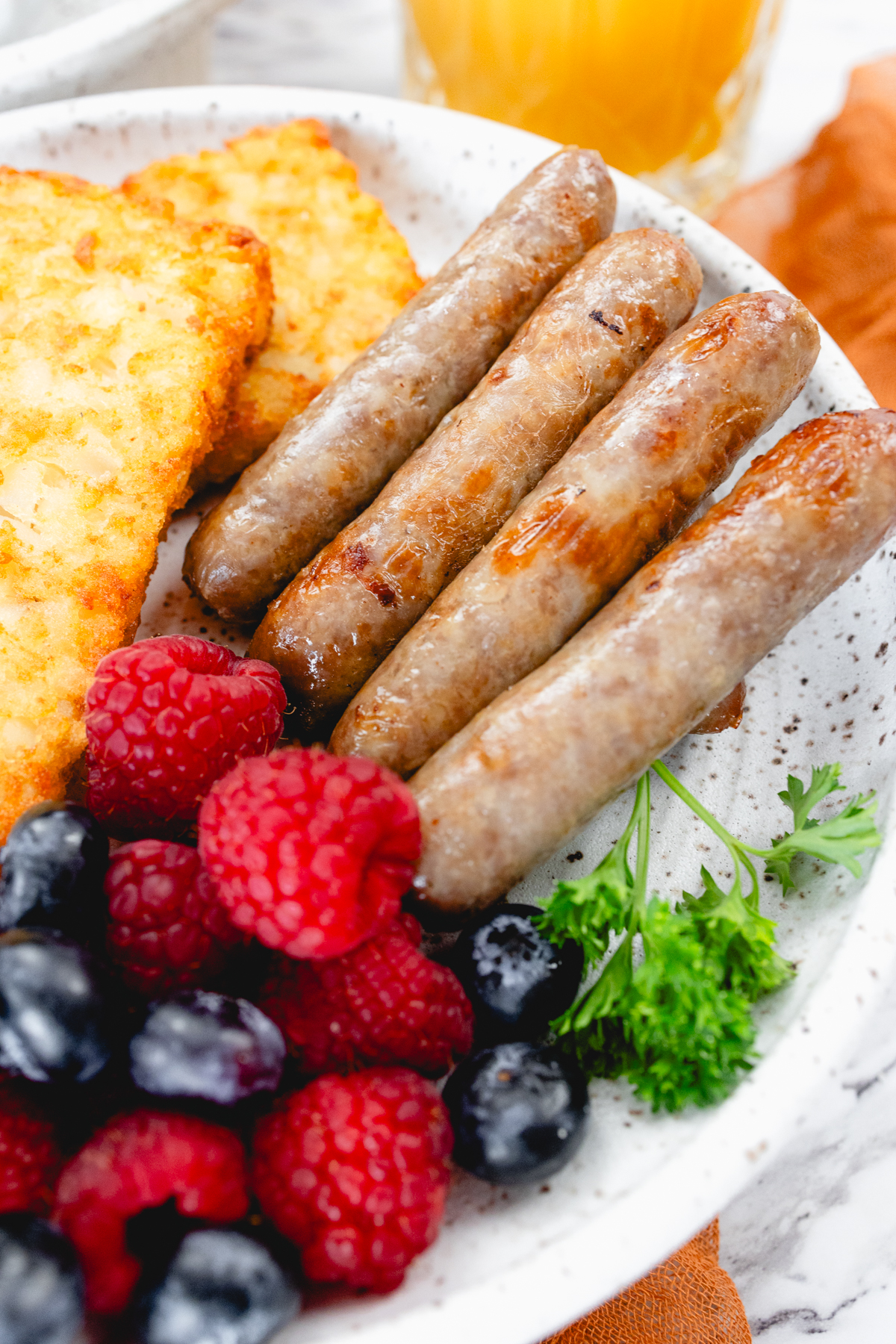 A close up view of link sausages on a white plate with berries and hash browns.