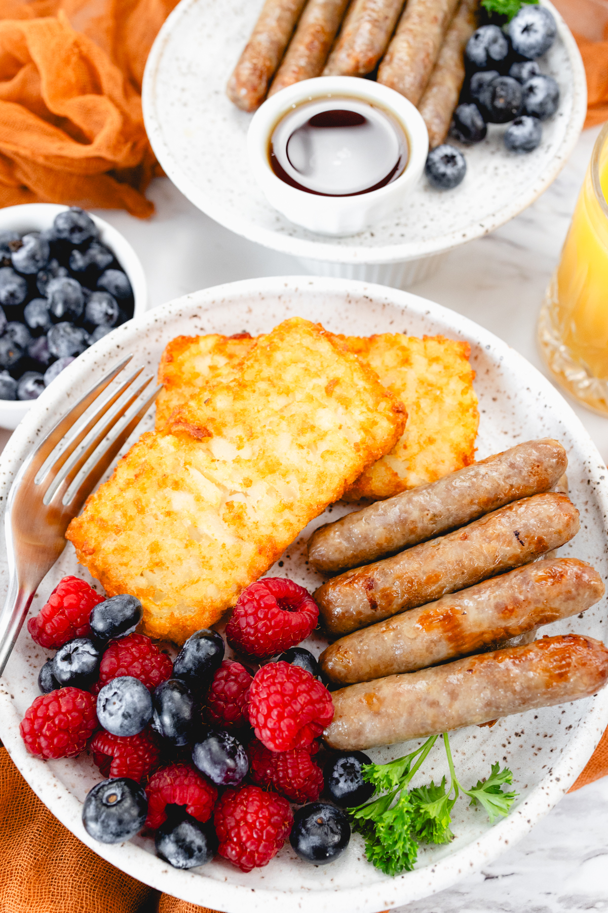 A top view of link sausages on a white plate with berries and hash browns.