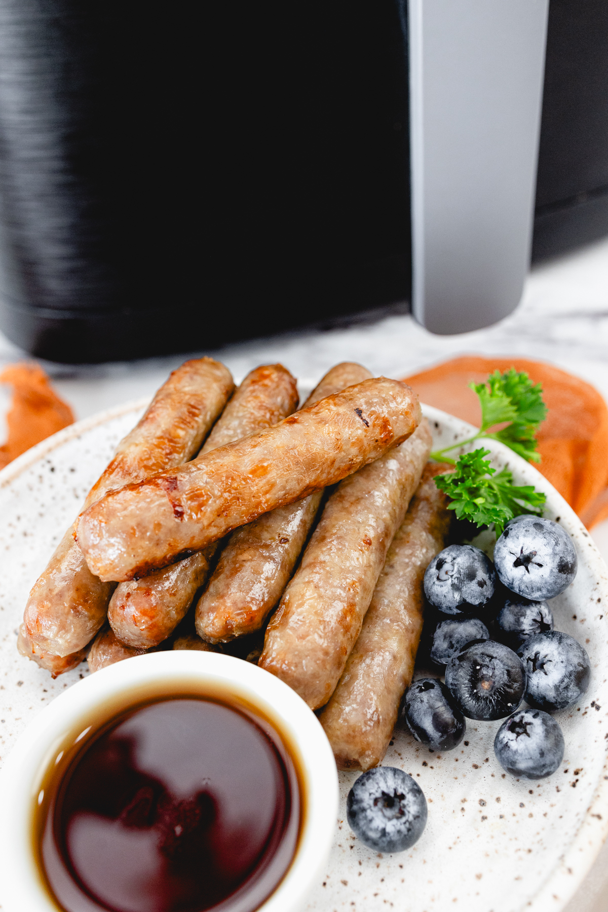 A top view of link sausages on a white plate with berries and gravy next to other breakfast items on a table.