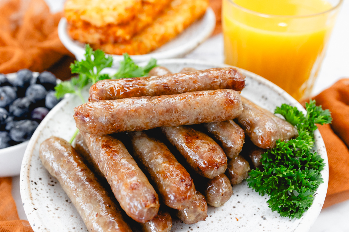 A top view of link sausages on a white plate with berries and gravy next to other breakfast items on a table.