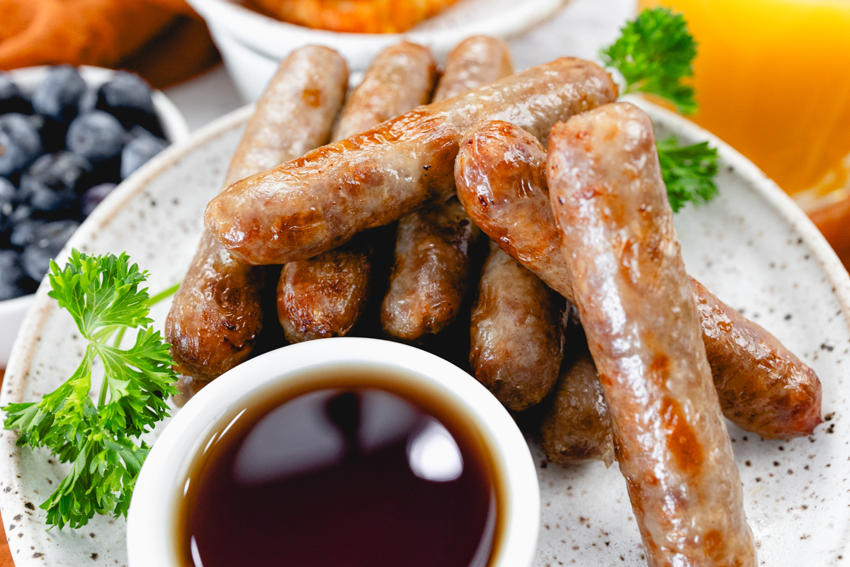 A top view of link sausages on a white plate with berries and gravy next to other breakfast items on a table.