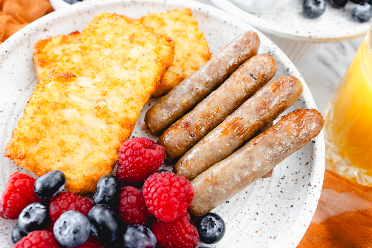 A close up view of link sausages on a white plate with berries and hash browns.