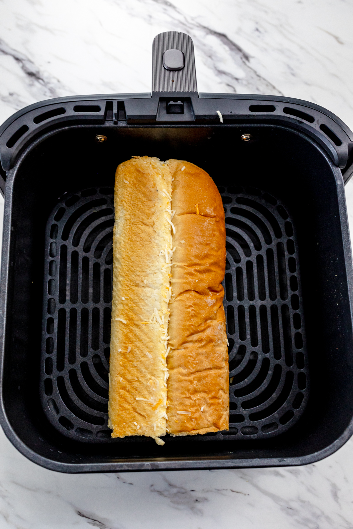 Top view of a garlic bread loaf in an air fryer basket.