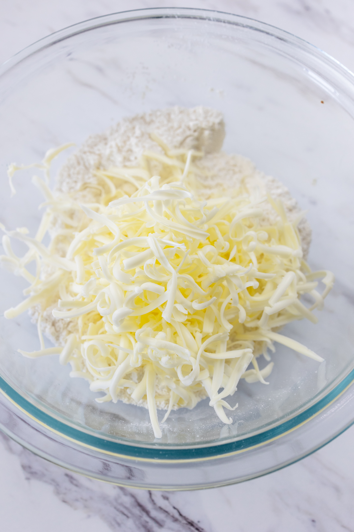 Top view of dry ingredients with grated butter on top in a glass mixing bowl.