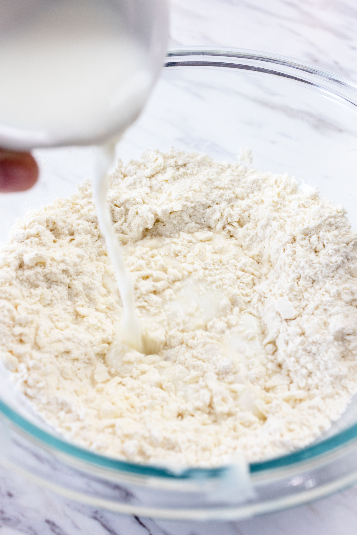 Close up view of dry ingredients in a glass mixing bowl with milk being poured into it.