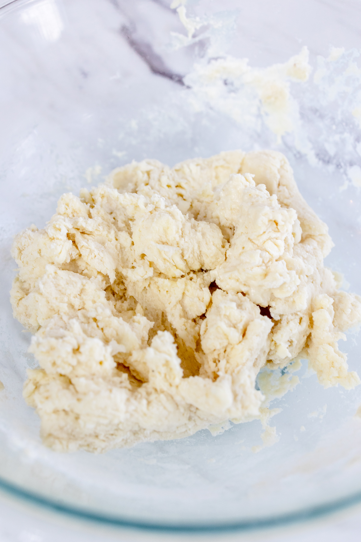 Top view of the biscuit dough coming together, in a glass mixing bowl.