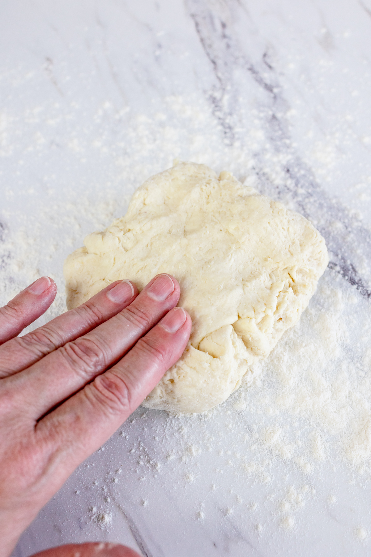 Top view of a hand pressing biscuit dough on a white surface.