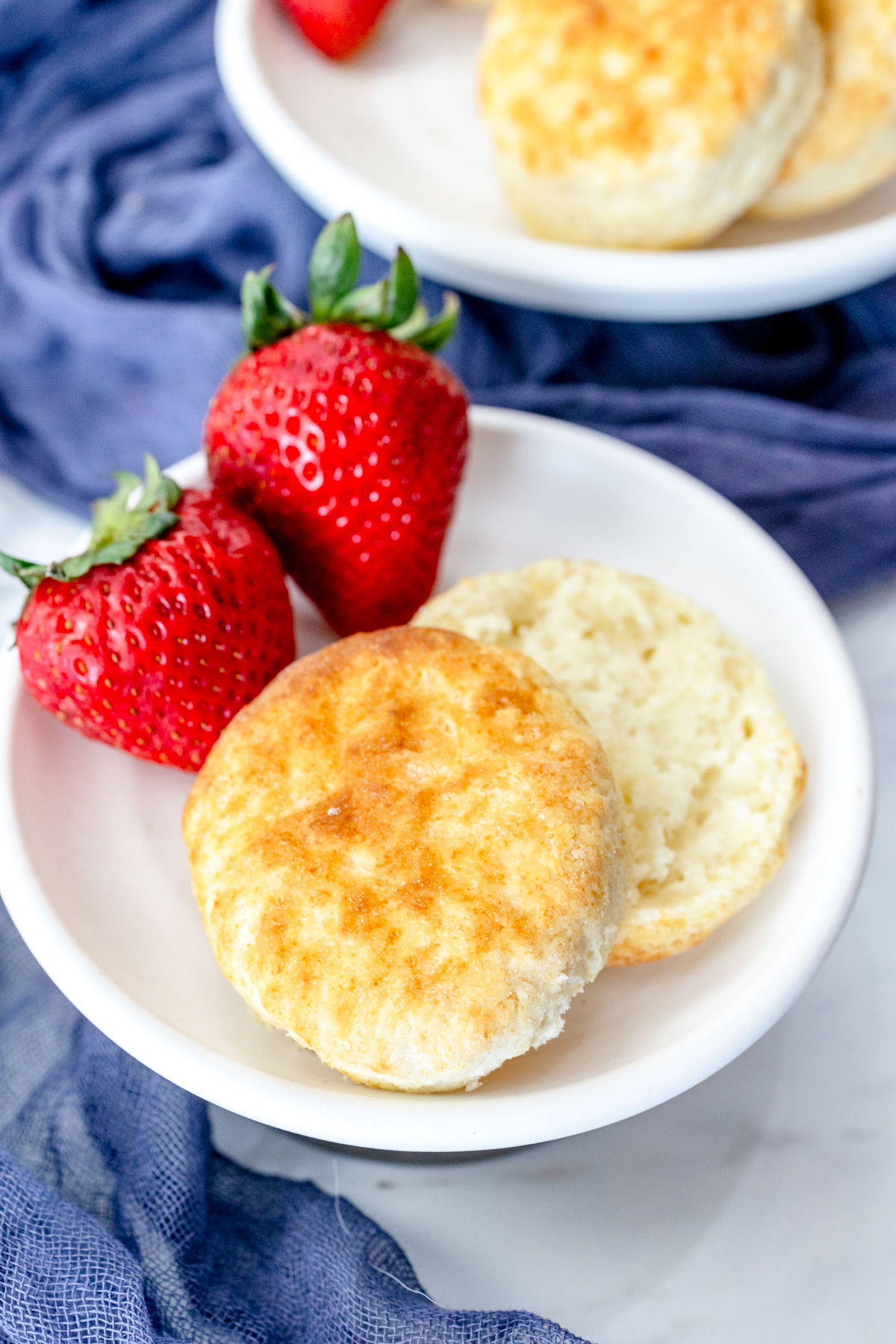 Medium-close view of a cooked Air Fryer Biscuit, sliced open, on a white plate with strawberries on the side.