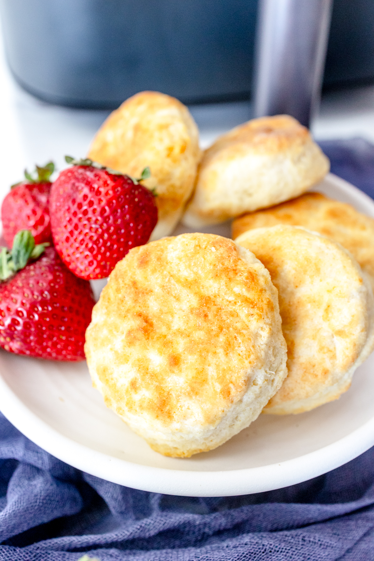 Medium-close view of cooked Air Fryer Biscuits, on a white plate with strawberries on the side, in front of an air fryer.