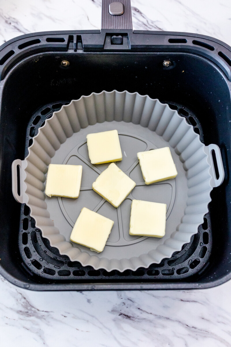 A top view of a silicone baking dish with butter cubes in it, in an air fryer.