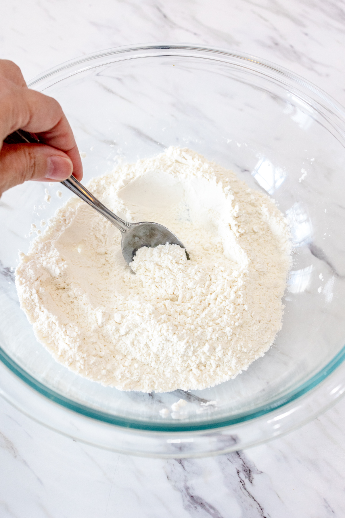 Close up image of someone making a well in the middle of the dry ingredients for butter swim biscuits with a spoon.