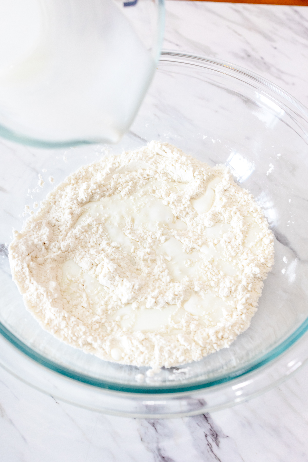 Close up image of buttermilk being poured into a well in the middle of the dry ingredients for butter swim biscuits.