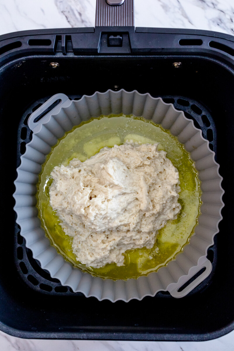 A top view of a silicone baking dish in an air fryer with melted butter and biscuit dough in it.