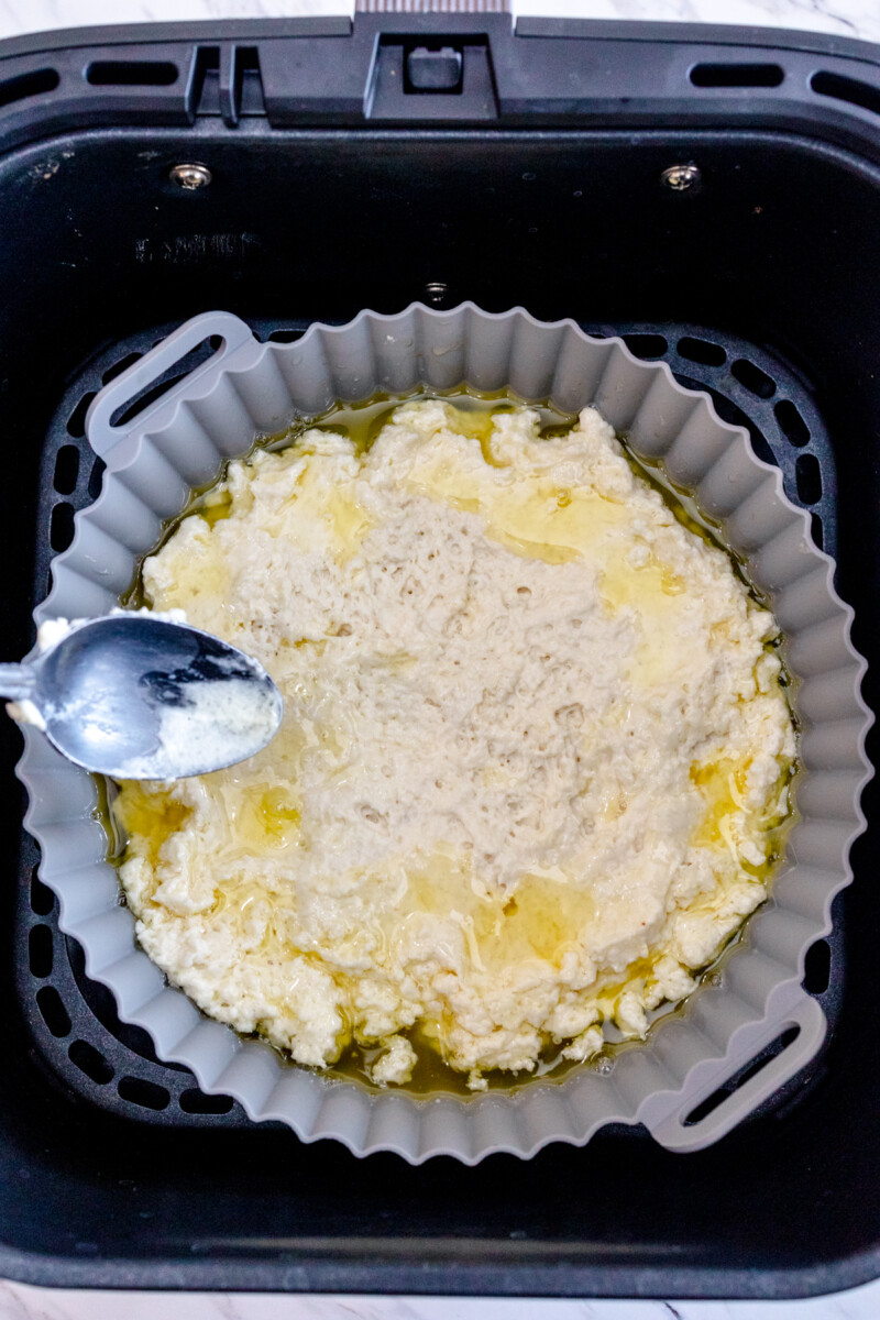 A top view of a silicone baking dish in an air fryer with melted butter and biscuit dough in it.