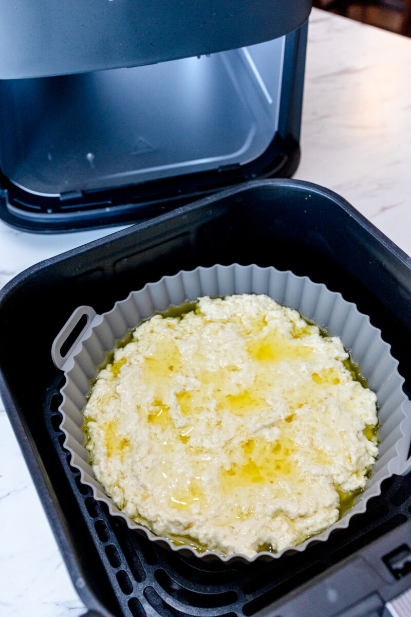 A close up view of a silicone baking dish in an air fryer with melted butter and biscuit dough in it.