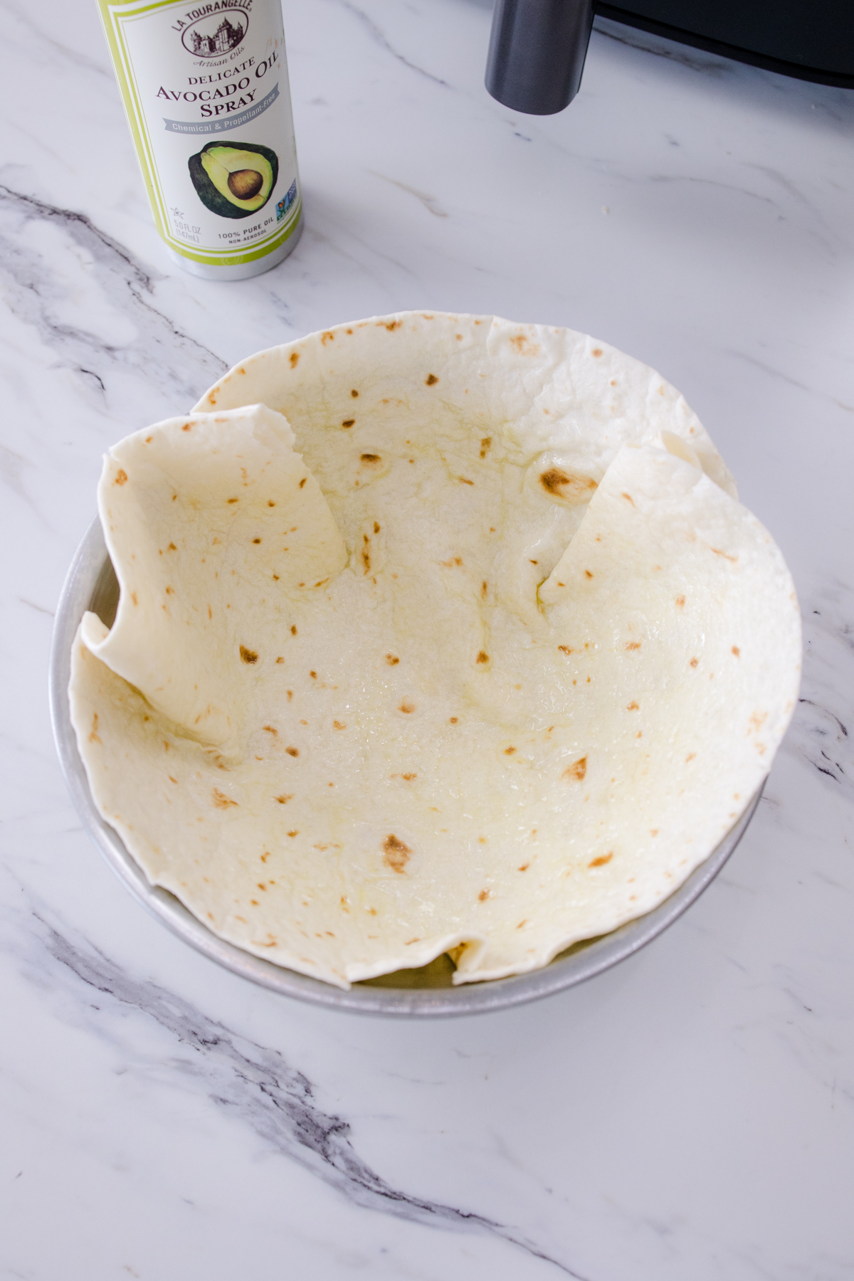 A flour tortilla in a metal bowl on a white surface.