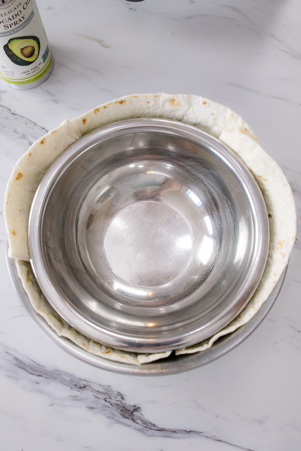 A tortilla between two metal bowls on a white surface.