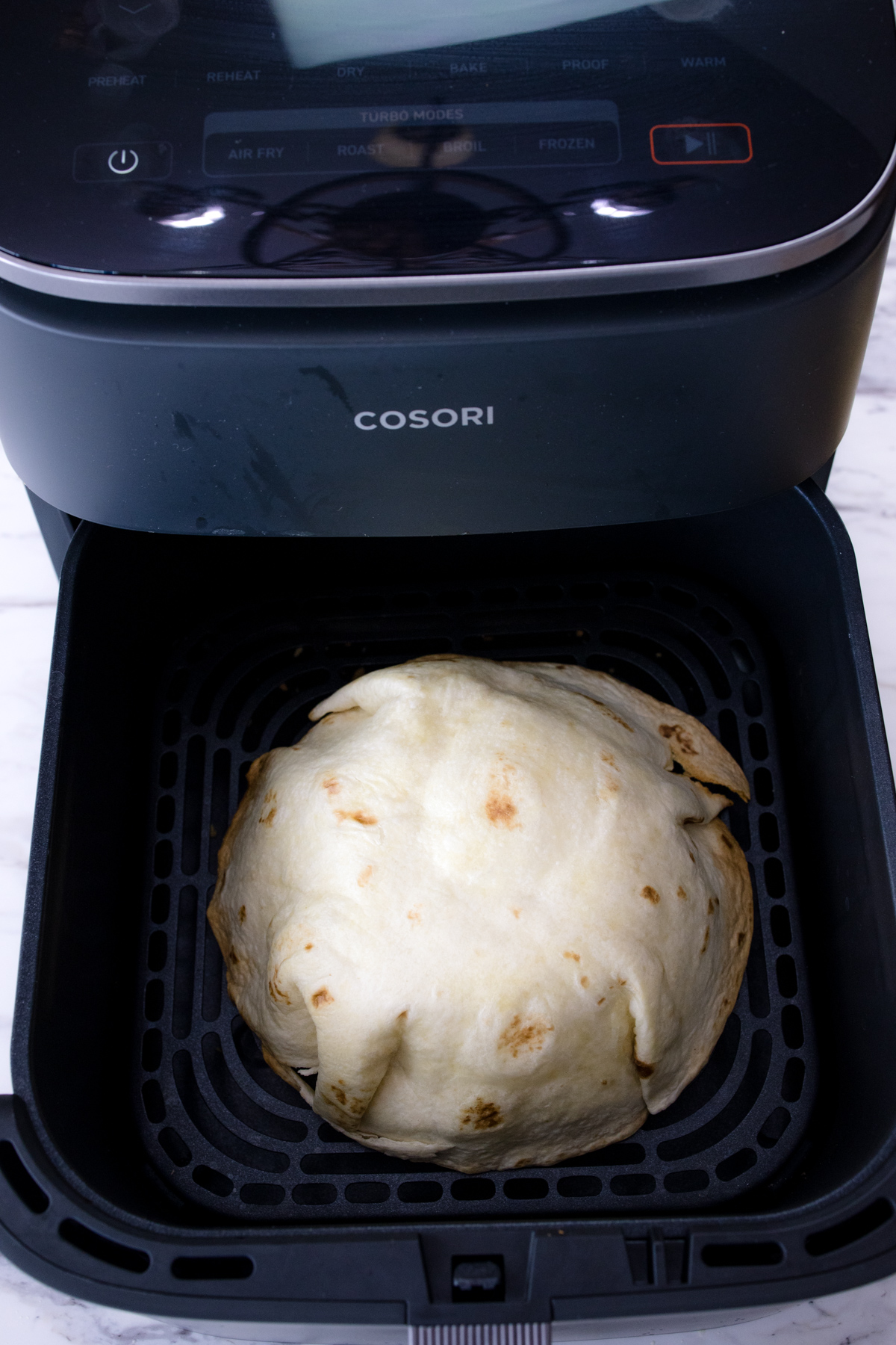 A partially cooked tortilla placed upside-down in an air fryer basket.