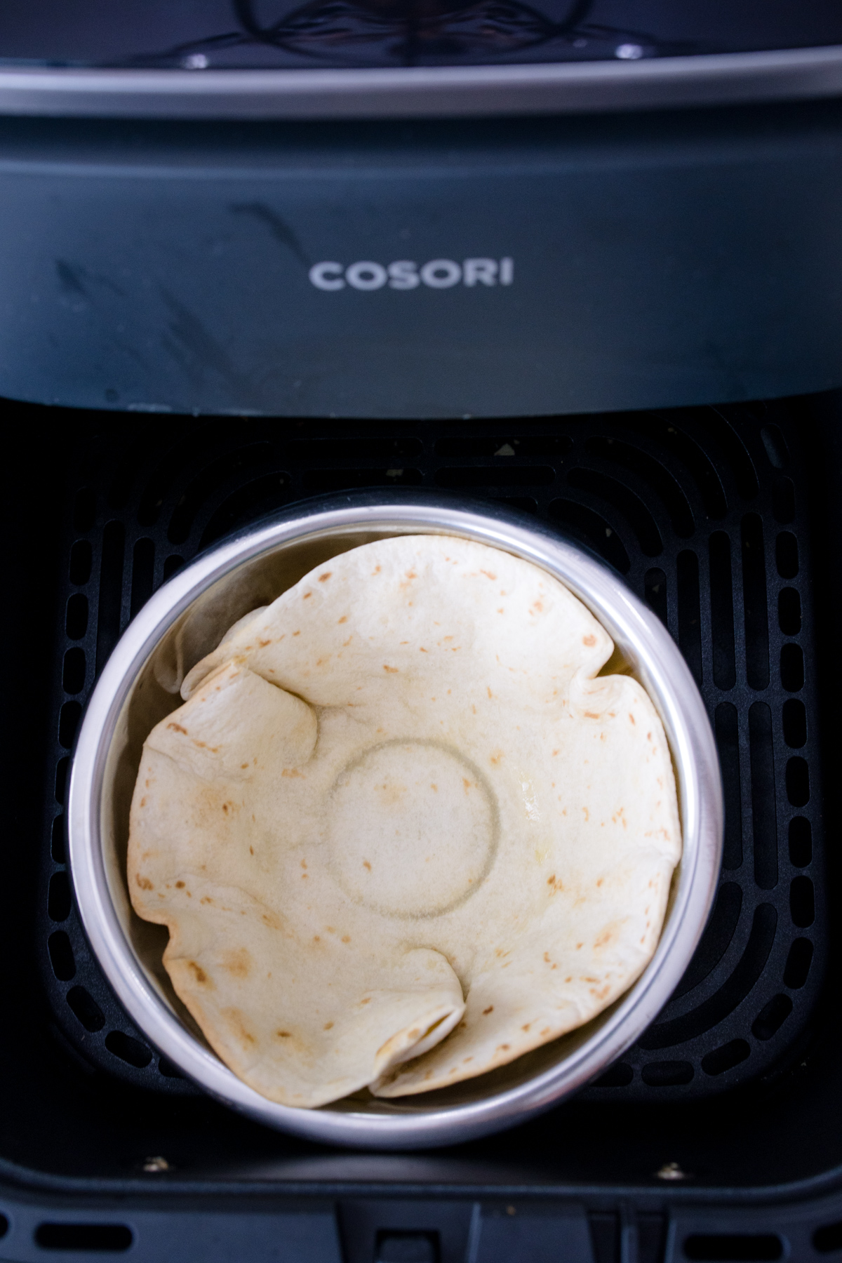 An uncooked tortilla in a metal bowl in an air fryer basket.