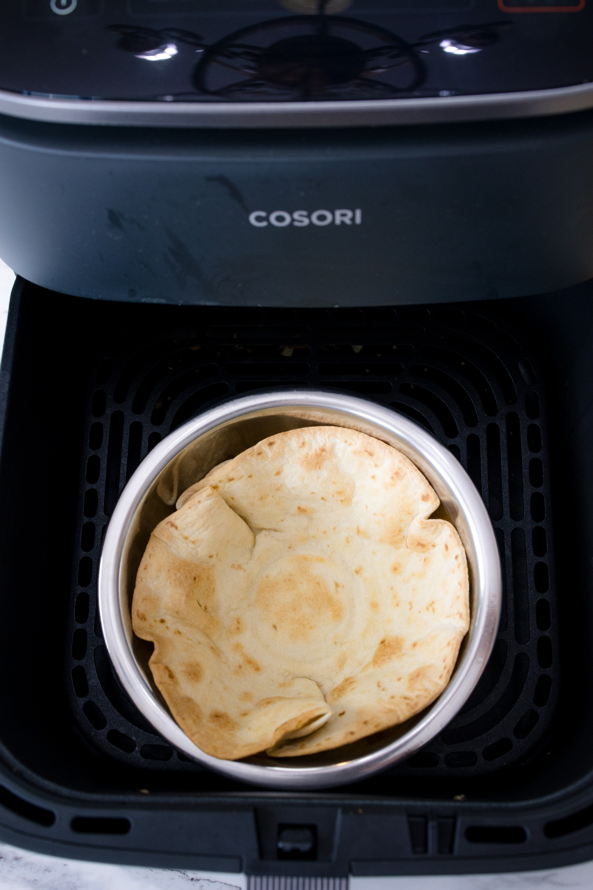 An cooked tortilla in a metal bowl in an air fryer basket.