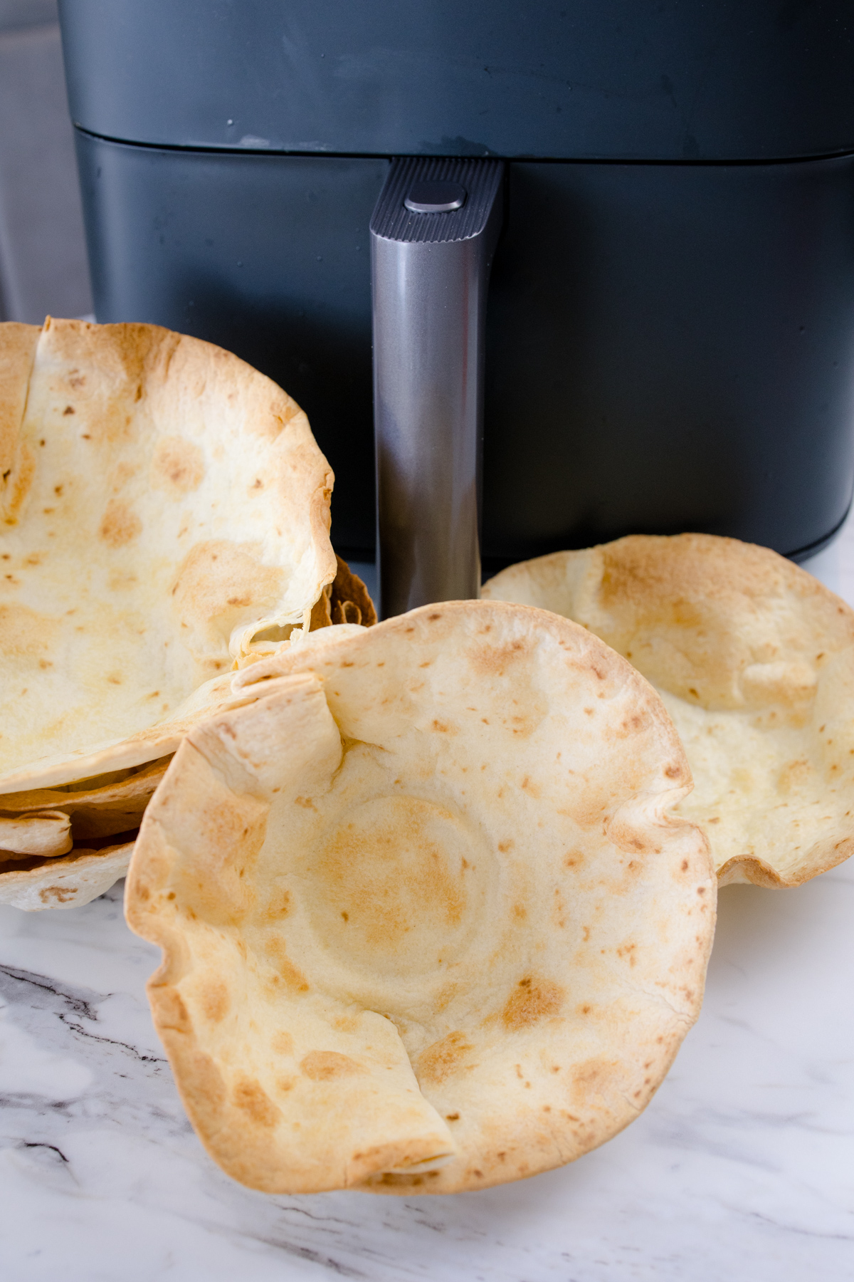 An assortment of Air Fryer Flour Tortilla Bowls in front of an air fryer.